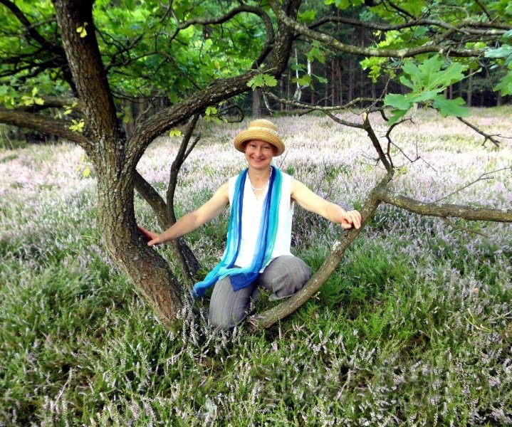 Heilpraktikerin Carla Neß sitzt auf einem Baumstamm. Sie lächelt.